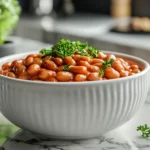 Stylish presentation of baked beans in a white ceramic bowl with fresh garnishes in a modern kitchen setting